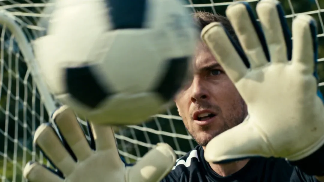 Goalkeeper's gloved hands deflecting a powerful shot.